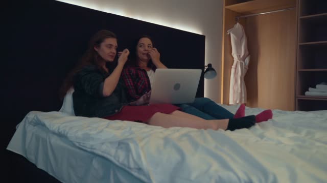 Zwei-attraktive-junge-Frauen-im-Bett-zu-Hause-mit-Laptop.-Freundschafts--oder-Frauenpaarkonzept