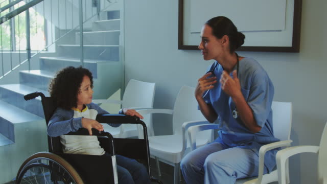 Vista-frontal-de-la-doctora-caucásica-interactuando-con-un-niño-discapacitado-en-el-pasillo-del-hospital-4k