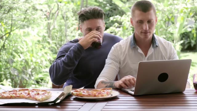 Pareja-gay-comandando-pizza-para-el-almuerzo.-Escribir-en-el-ordenador-portátil.