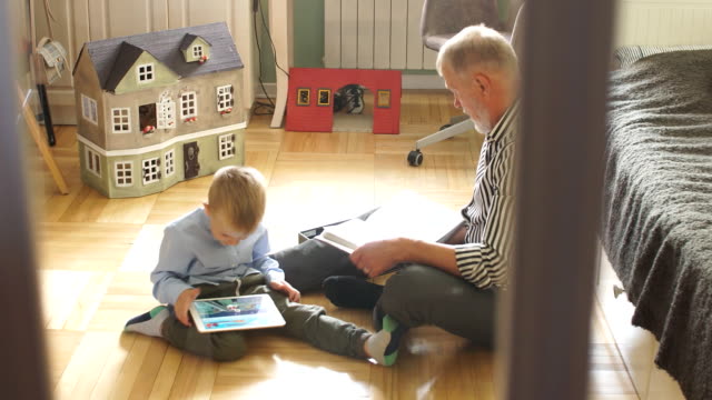 Grandpa-looks-photo-album-with-his-wedding,-little-boy-using-electronic-tablet
