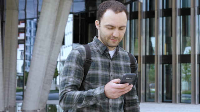 Casual-Man-Walking-near-the-Modern-Building-and-using-smarphone-smiling