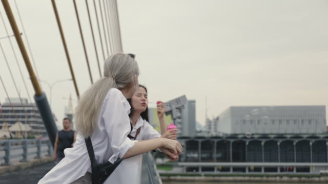 Asiatische-lesbische-Paare-spielen-Seifenblasen,-während-sie-auf-der-Brücke-stehen.