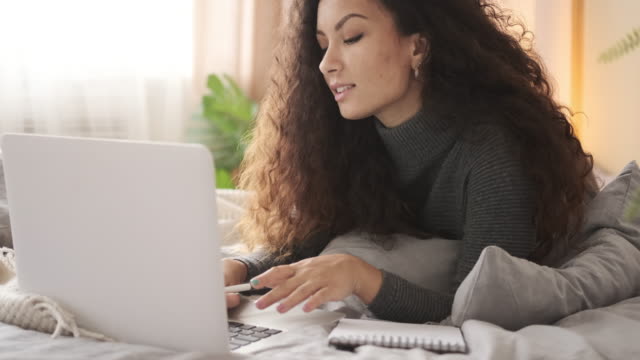 Mujer-usando-computadora-portátil-y-escribiendo-notas-en-la-cama