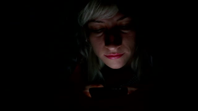 Fröhliche-junge-Frau-mit-Smartphone-unter-der-Decke-im-Bett-und-lächelte