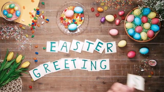 Man-puts-words-Easter-Geetings-on-table-decorated-with-easter-eggs.-Top-view