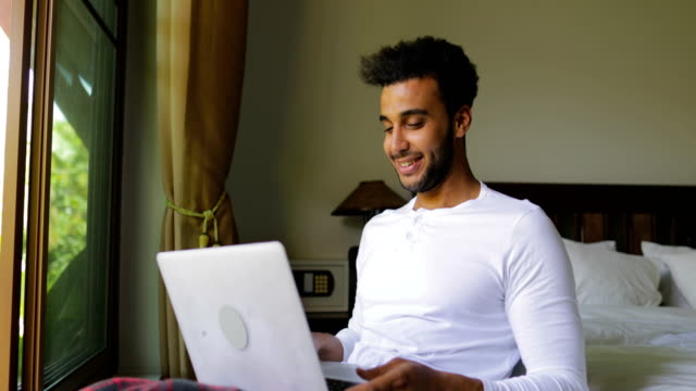 Hispanische-Jüngling-mit-Laptop-Computer-glücklich-lächelnden-Mann-im-Chat-Online,-über-große-Fenster-mit-Blick-auf-den-tropischen-Garten