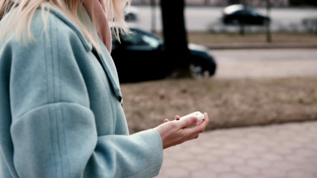 Slow-motion-blonde-woman-in-blue-coat-texting.-Side-view.-Girl-sending-messages-on-the-go.-Lifestyle.-High-pace-of-life