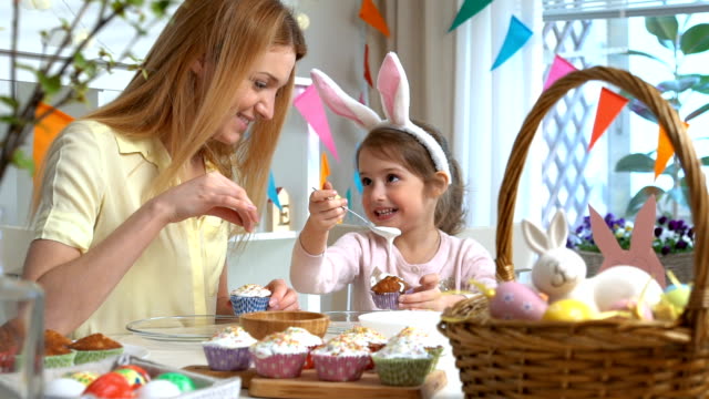 Joven-madre-y-su-hija-con-orejas-de-conejo-cocinar-cupcakes-de-Pascua