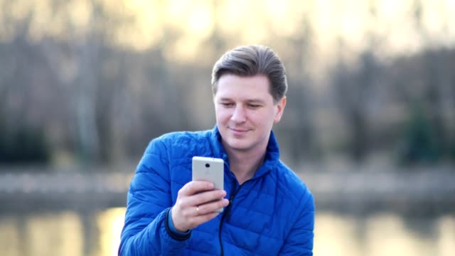 Un-hombre-atractivo-joven-está-utilizando-un-teléfono-móvil-al-atardecer.