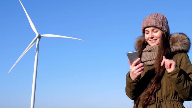 Internet-chatting,-nice-female-sits-in-social-networks-using-mobile-phone-beside-windmill