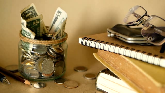 Books-with-glass-penny-jar-filled-with-coins-and-banknotes.-Tuition-or-education-financing-concept.-Scholarship-money.