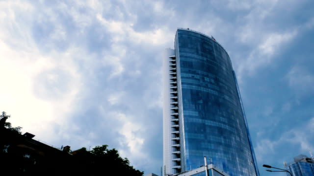Vídeo-de-lapso-de-tiempo.-Una-vista-desde-abajo-en-un-centro-de-negocios-de-vidrio-sobre-un-fondo-de-nubes-grises-en-movimiento