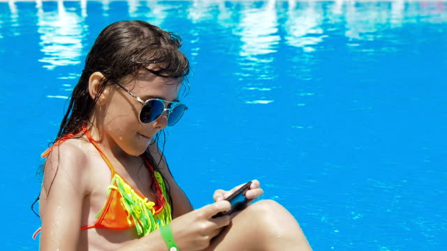Ein-Kind-spielt-mit-einem-Handy-in-den-Pool.