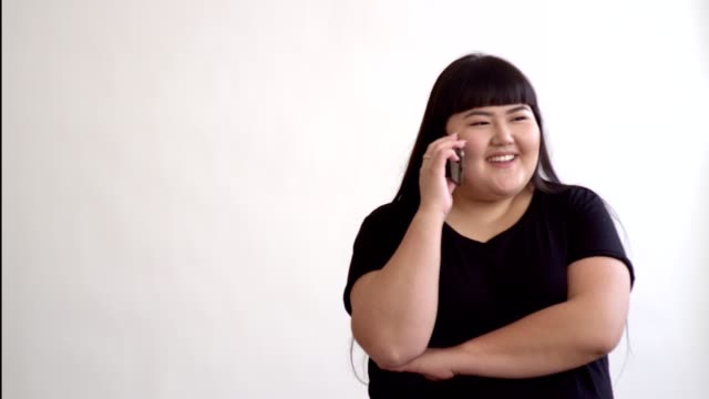 Plus-Size-Mädchen-mit-Telefon-im-Gespräch-auf-weißem-Hintergrund.-Asiatische-Mädchen-Lächeln-auf-den-Lippen-und-am-Telefon-sprechen