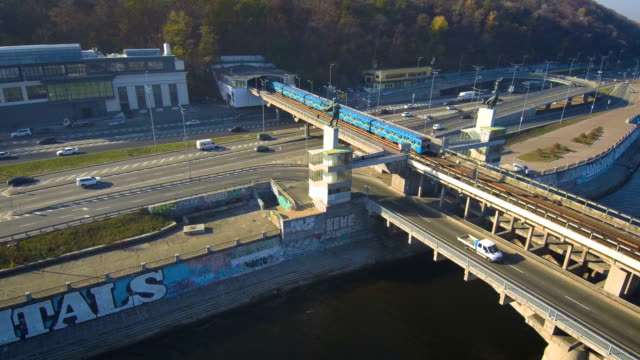 Vista-aérea,-superior-de-Drone:-Metro-tren-viaja-a-través-de-un-puente-con-autos-y-camiones.