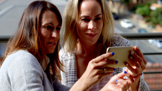 Lesbian-couple-using-mobile-phone-in-balcony-4k