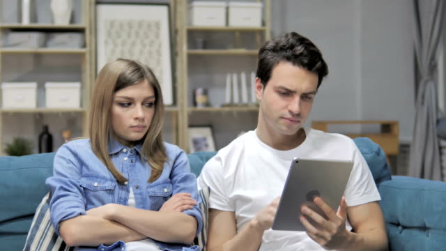 Man-Using-Tablet-while-Angry-Grilfriend-Sitting-Aside-on-Couch