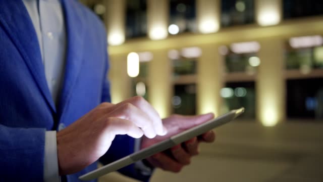 Hands-of-businessman-using-tablet-computer-in-night-street,-close-up-of-man-tapping-and-swiping-touchscreen-while-browsing-Internet-outdoors