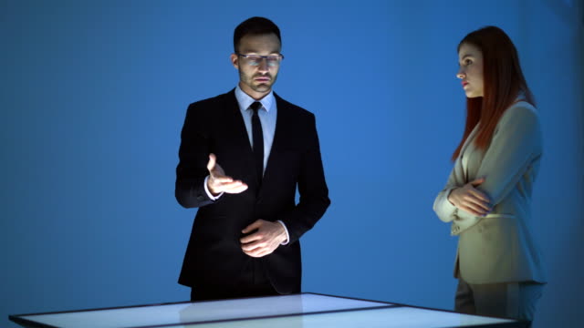 Der-Geschäftsmann-und-eine-Frau,-die-mit-einem-virtuellen-Display-auf-blauem-Hintergrund-arbeiten