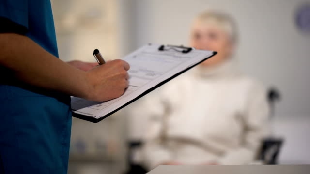 Therapist-making-notes-in-medical-records-and-examining-elderly-lady,-hospital