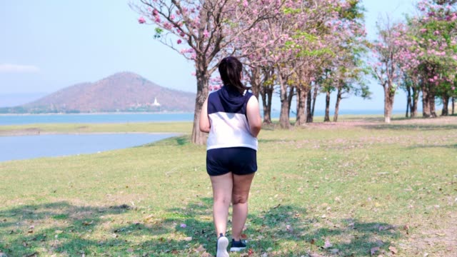 Una-mujer-asiática-gorda-que-trota-en-la-luz-del-sol-natural-por-la-mañana.
Ella-está-tratando-de-perder-peso-con-el-ejercicio.--concepto-de-salud-con-ejercicio.