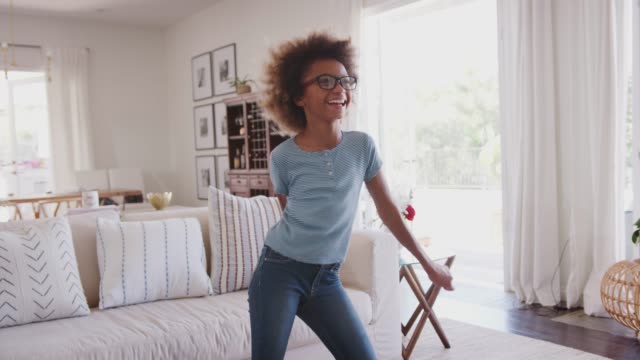 Pre-adolescente-chica-sosteniendo-smartphone-y-bailando-a-la-música-en-la-sala-de-estar-en-casa,-de-cerca