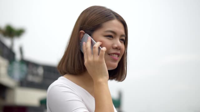 Hermosa-mujer-asiática-hablar-con-el-teléfono-celular-al-lado-del-río.-Close-up-cara-atractiva-y-alegre-joven-asiática-femenina.