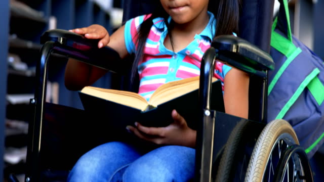 Vista-frontal-de-la-colegiala-afroamericana-discapacitada-leyendo-un-libro-en-la-biblioteca-en-la-escuela-4k