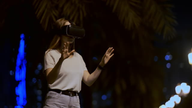 Junge-Frau-in-Virtual-Reality-Brille-in-der-Nachtstadt-bewegt-ihre-Hände