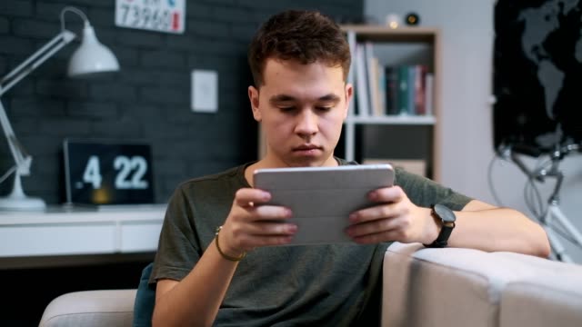 Nahaufnahme-Porträt-eines-Teenagers,-der-zu-Hause-auf-seinem-Tablet-spielt,-schaut-in-die-Kamera-am-Ende