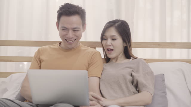 Asiatische-paar-mit-Laptop,-während-auf-dem-Bett-liegen,-wenn-im-Schlafzimmer-entspannen,-Paar-spielen-Social-Media-in-Computer-zu-Hause.-Paar-mit-Entspannung-Zeit-zu-Hause-Konzept.