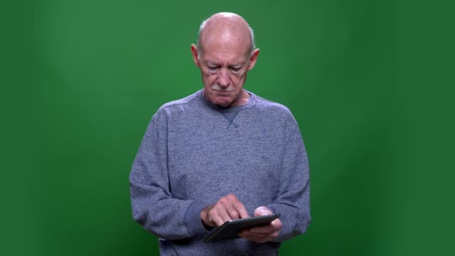 Closeup-shoot-of-old-senior-caucasian-man-using-the-tablet-looking-at-camera-with-background-isolated-on-green