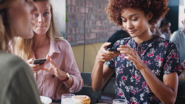Gruppe-junger-Freundinnen-trifft-sich-und-sitzt-am-Tisch-Fotos-von-Lebensmitteln-auf-Mobiltelefonen,-um-in-sozialen-Medien-zu-posten---in-Zeitlupe-gedreht