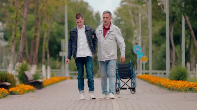 Dad-helps-disabled-son-to-go,-family-support.-Disabled-guy-walking-down-the-road.