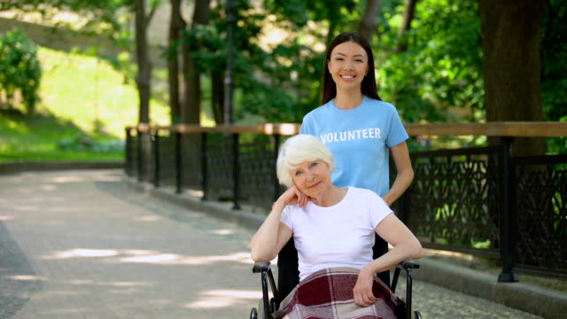 Lächelnde-weibliche-Freiwillige-und-behinderte-Seniorin-suchen-Kamera,-Nächstenliebe