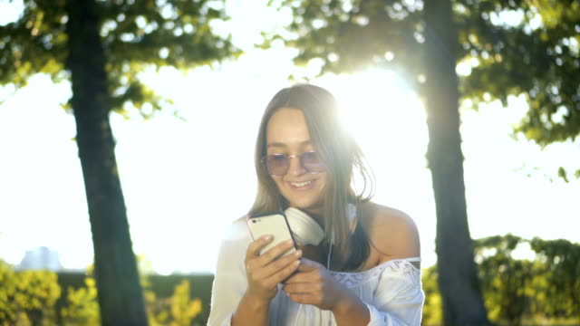 Junge-Frau-draußen-im-Park-lächelnd-und-SMS-auf-dem-Smartphone