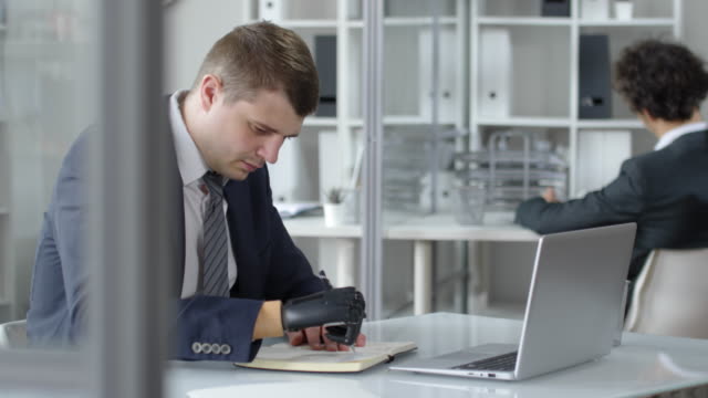 Businessman-with-Prosthetic-Hand-Writing-in-Notepad-at-Office-Desk