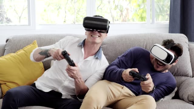 Gay-couple-relaxing-on-couch-playing-virtual-reality-games.-Exciting-mood.-Interesting-mood.-Fun-action.