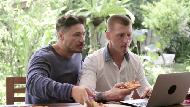 Gay-couple-having-pizza-for-lunch.-Concentrated..