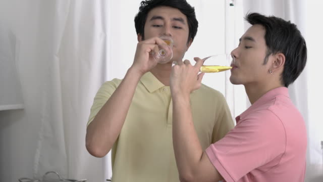 Asian-couple-gay-celebrating-at-home.-Gay-boy-drinking-beverage-for-happy-emotion-love-anniversary-together.-Concept-of-lifestyle,-family,-gay-and-bisexual.