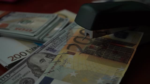 The-stapler-fastens-the-dollar-and-euro-notes-with-iron-clips.-Stapler-with-paper-clips-on-the-background-of-banknotes.-Counterfeit-money