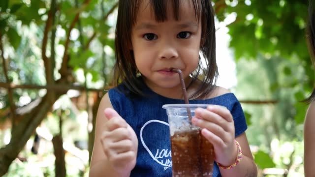 Little-Asian-child-girl-sipping-her-drink-while-sitting-rest-in-the-park-on-summer-day.-Selective-focus.
