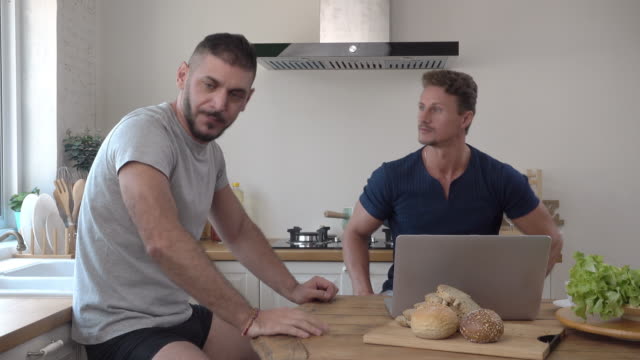 Gay-male-couple-arguing-impatiently-while-using-notebook-computer-at-table