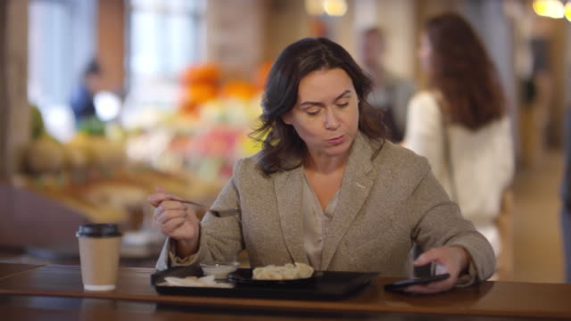 Mujer-usando-Smartphone-mientras-almuerza-en-el-mercado-de-alimentos