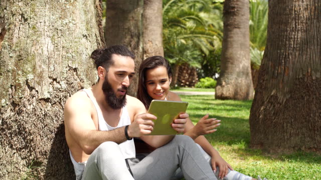 Man-and-woman-relaxing-with-digital-tablet-in-park-after-sports-training