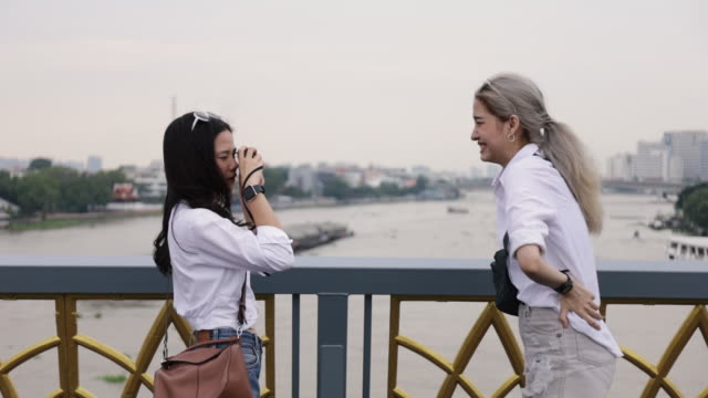 Happy-Asian-lesbian-couple-taking-a-photo-while-standing-on-the-bridge.-Beautiful-Asian-women-traveling-with-a-friend's-vacation-lifestyle.