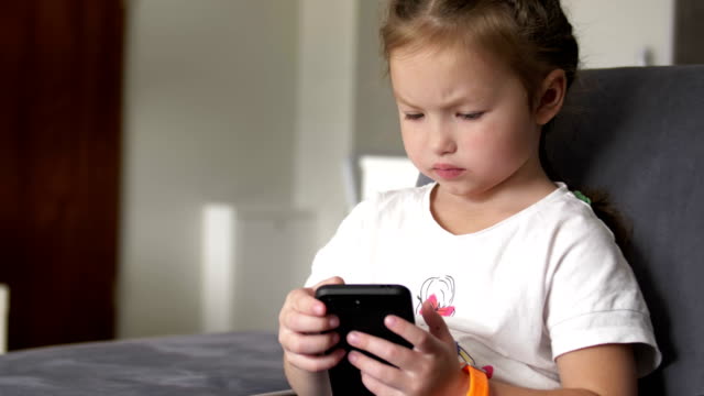 Casual-child-sitting-on-a-couch-at-home,-playing-and-touching-a-mobile-phone