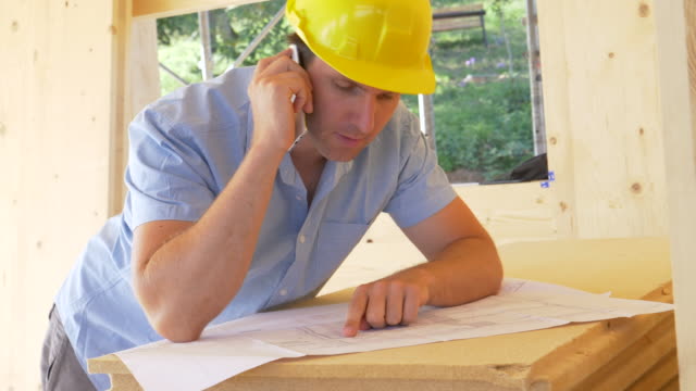 CERCA:-El-joven-gerente-del-sitio-de-construcción-discute-los-planos-de-piso-por-teléfono.