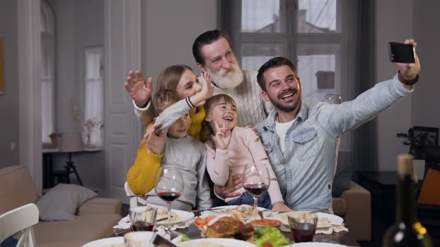 Close-up-of-joyful-pleasant-family-which-sitting-around-the-dinner-table-and-making-selfie