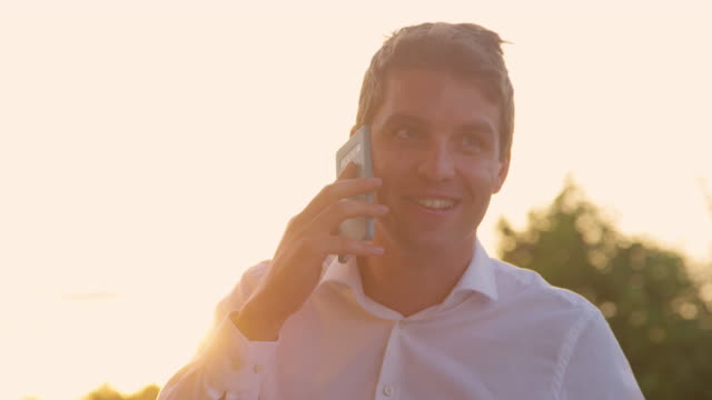 CLOSE-UP:-Erfolgreicher-Geschäftsmann-spricht-bei-goldenem-Sommersonnenuntergang-am-Telefon.